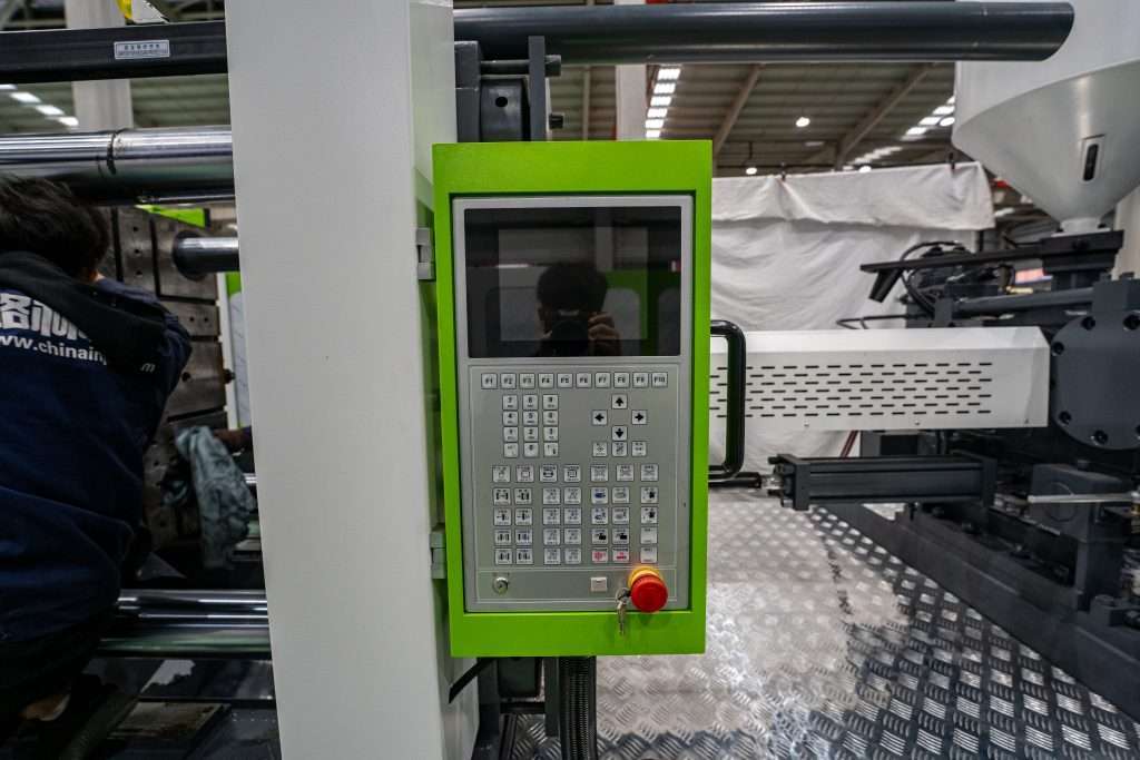 Operator inspecting an injection molding machine control panel and clamping unit